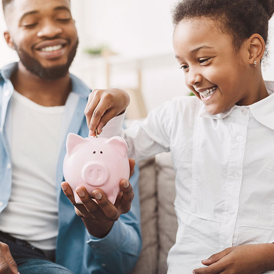 Father and daughter putting money in piggy bank