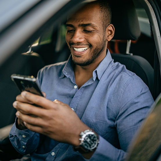Young man sitting using phone in new car