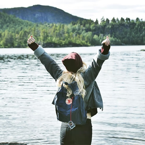 Woman standing in front of lake with hands raised
